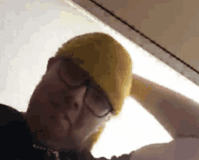 a man wearing glasses and a yellow hat looks down at something