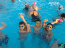 a group of children are swimming in a pool and one of them is wearing a pink swim cap with the letter s on it