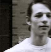 a black and white photo of a man with a brick wall in the background