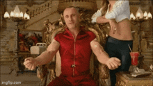 a man in a red shirt is sitting in a chair with his arms outstretched in front of a woman .