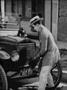 a man in a suit and hat is standing next to an old car on the side of the road .