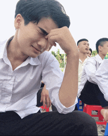 a young man in a white shirt is covering his face with his hand