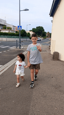 a boy and a girl are walking down a street with a crosswalk sign above them