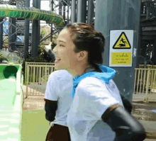 a woman is standing in front of a water slide at a water park with a yellow sign that says caution