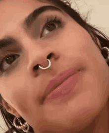 a close up of a woman with a nose ring and earrings .