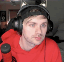 a man wearing headphones and a red hoodie looks at the camera