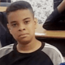 a young boy is sitting at a desk in a classroom and making a funny face .