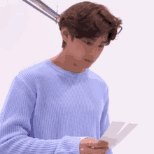 a young man in a blue sweater is holding a piece of paper in his hand .