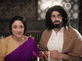 a woman in a purple sari and a man with a beard are posing for a picture with the letters nn visible