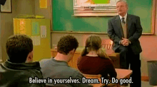 a man in a suit and tie is standing in front of a group of students in a classroom and talking to them .