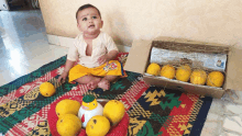 a baby sits on a colorful rug next to a box of fruit