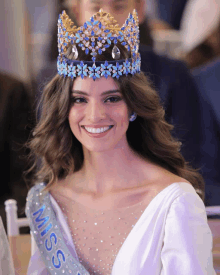 a woman wearing a crown and a miss sash smiles for the camera