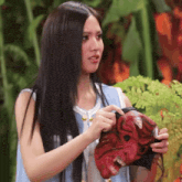 a woman with long black hair is holding a red demon mask