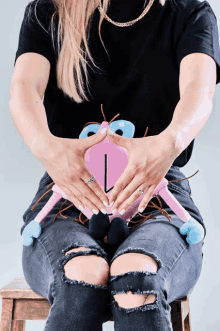 a woman is sitting on a stool holding a stuffed animal with her hands