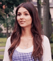 a woman with long hair is standing in a park wearing a white shirt and a blue and white checkered dress .