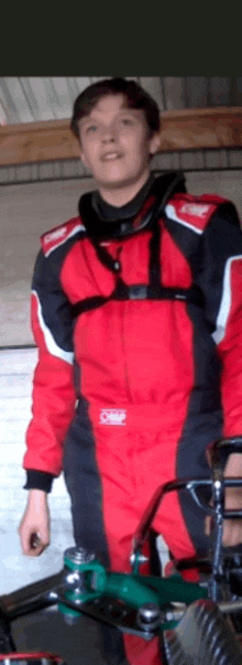 a man in a red and black omp racing suit stands in a garage