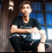 a man wearing a black t-shirt with a white square on it is squatting down