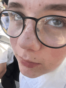 a close up of a person 's face with glasses and a white shirt on