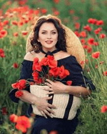 a woman is sitting in a field of red flowers holding a basket of red flowers .