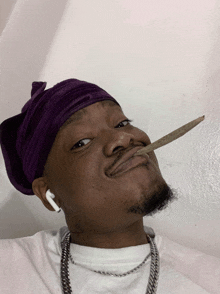 a man wearing a purple bandana holds a cigarette in his mouth