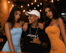 a man wearing a black lacoste shirt stands with two women