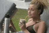 a woman in a bikini drinking a drink through a straw