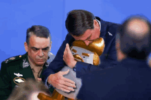 a man in a suit holds a gold object in front of a blue background