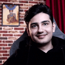 a young man is smiling in front of a brick wall with a picture of a woman in the background