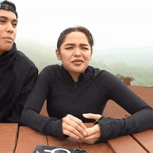 a man and a woman are sitting at a picnic table and the woman is wearing a black shirt with the letter o on it