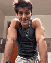 a young man wearing a tank top and a necklace smiles for the camera