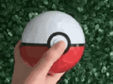 a person is holding a red and white pokeball with their finger .