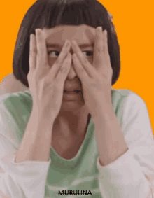 a woman is covering her face with her hands .