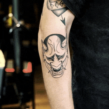 a man has a black and white tattoo of a demon mask on his arm .