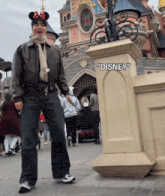 a person wearing minnie mouse ears stands in front of a disney statue