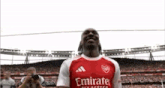 a soccer player in a red and white emirates jersey is standing in front of a crowd .