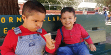 two young boys eating ice cream on a green bench that says " orm " on it