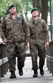 two soldiers are walking across a wooden bridge and one of them has a green beret