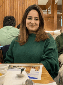 a woman in a green sweater sits at a table in front of a menu