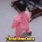 a baby in a pink outfit is walking in front of a startamilchat.in logo
