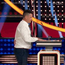 a man in a white shirt and tie is standing in front of a podium with the words family feud canada written on it