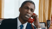 the man is wearing a suit and tie and talking on a red telephone .