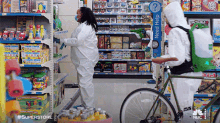 a man is riding a bike in a store while a woman in a protective suit stands next to him .