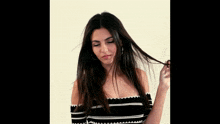 a woman in a black and white off the shoulder top is holding her hair