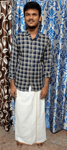 a young man wearing a plaid shirt and a white skirt is standing in front of a blue and white curtain .