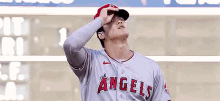 a baseball player for the angels is standing in front of a scoreboard and looking up at the sky .