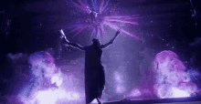 a person is standing on a stage with their arms outstretched in front of a purple light .