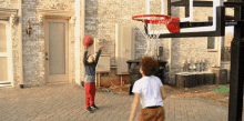 two boys are playing basketball in front of a brick house