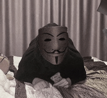 a person wearing a anonymous mask is laying on a bed holding money .