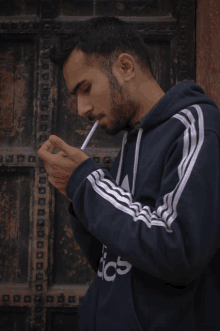 a man smoking a cigarette wearing an adidas hoodie