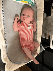 a baby in a red and white striped shirt is laying on a changing pad